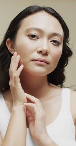 Vertical video of asian woman with dark hair on beige background, slow motion. Femininity, face, facial expressions, body, skin and beauty, unaltered.