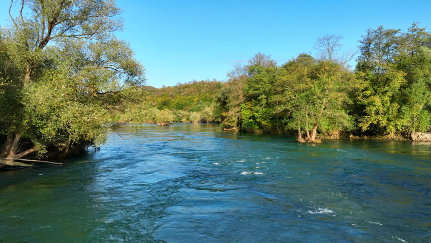 Turquoise water of a mountain river flowing downstream through a dense green forest on a sunny day. Una river, Bosnia and Herzegovina