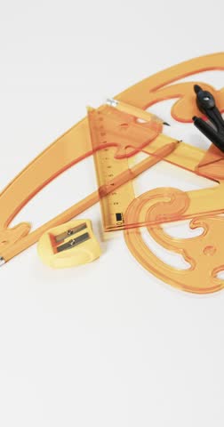 Vertical video of compass, pencil, sharpener, eraser and rulers on white background, slow motion. Geometry, design, learning and education concept.