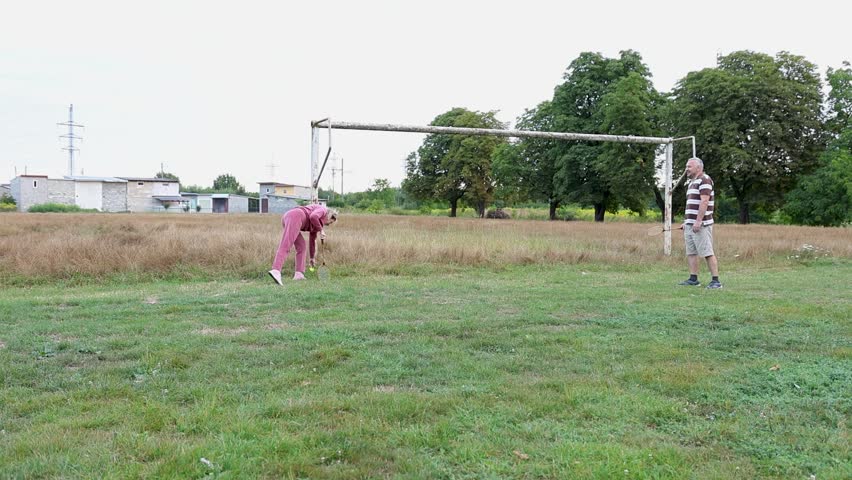 Two people playing badminton on a field near old football goalposts, enjoying active outdoor recreation.