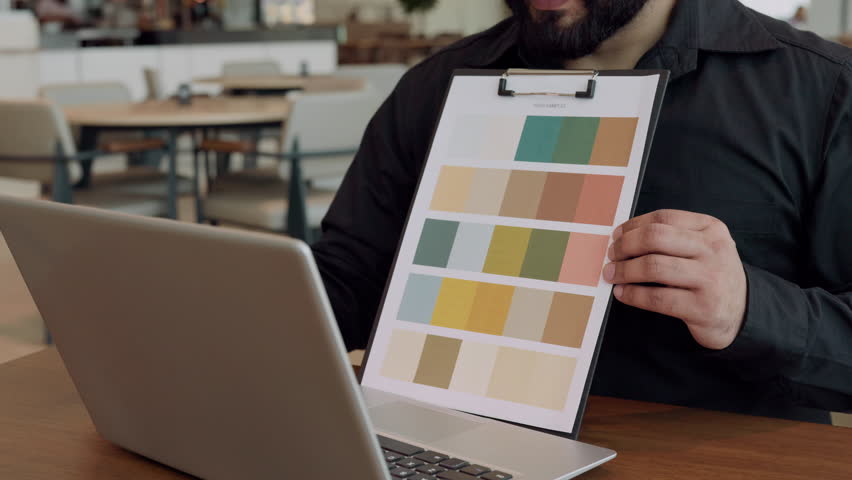 Closeup view of Indian designer shows colors palette to client at video call in office. Male architect discusses decor style of building via laptop at workplace. House renovation