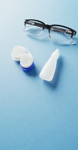 Vertical video of glasses and contact lenses with eye drops on blue backrgound with copy space. Medicine, healthcare and copy space concept digital composite video.