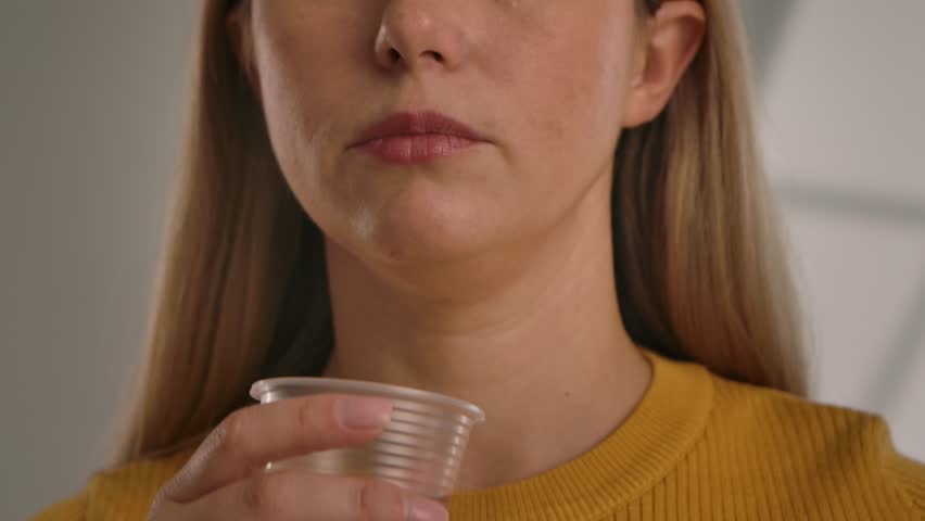 A woman rinses her mouth with water. An unrecognizable woman in a yellow sweater takes a sip of sparkling water and rinses her mouth, close up of her face. Slow motion.