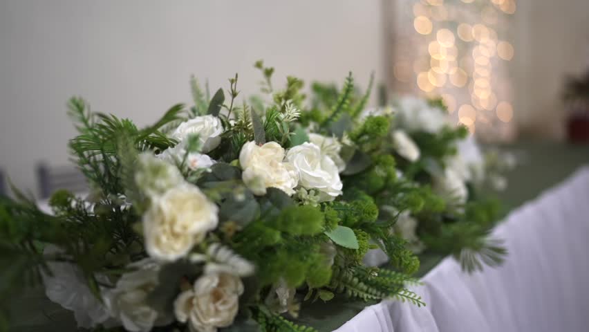 Parallax close-up of elegant wedding table centerpiece featuring white roses and lush green foliage decoration for a romantic celebration event
