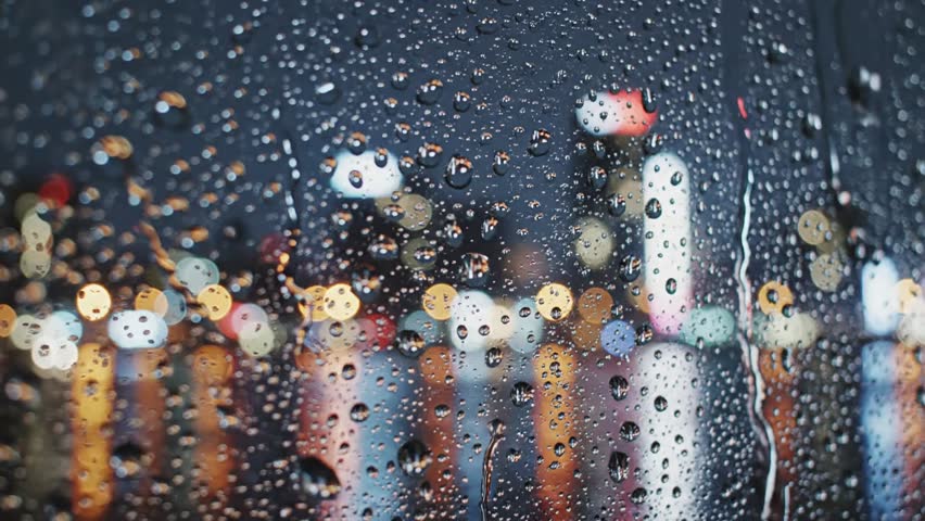 Cinematic video of raindrops on a window with blurred city lights in background. Cool blue-gray tone, calm ambience, realistic texture. Generated using AI (Veo3)