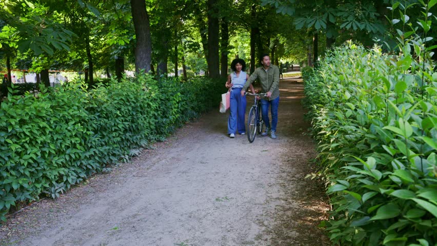 Happy multiracial couple enjoying a romantic walk in the park. Asian man and black woman talking and laughing together with a bicycle