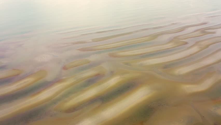 Cape Cod tidal flats at low tide reveal long sand ridges, shallow pools of seawater reflecting the sky, and dune grass bordering the beach in a timeless New England coastal scene.
