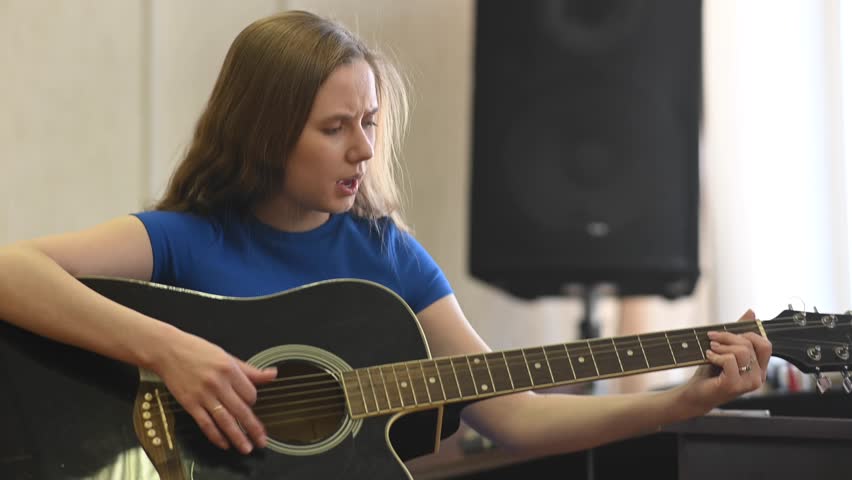 Young woman playing guitar in recording studio. 