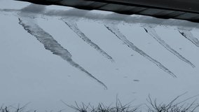 Close-up vertical shot of several large, clear icicles hanging from a roof edge during a heavy snowfall. The background is a bright, overcast sky with falling snow. Winter weather nature footage. - Powered by Shutterstock - Get 15% off with code: PIKWIZARD15