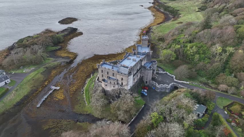 Aerial view of the historic Duart Castle with stone walls and green grass, standing proudly against the rugged coastline and lush forest, Scotland.