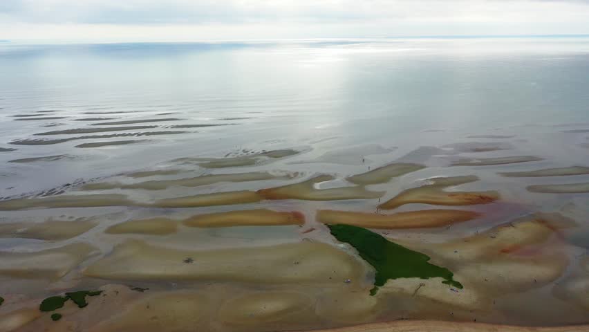 Nantucket coastline at low tide displays exposed sand ridges, tidal flats dotted with reflective tide pools, and dune grass adding texture along the edges of the sandy beach.
