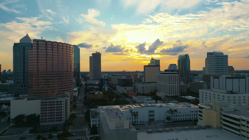 Tampa skyline as the sun begins to set and beautiful colors fill the sky illuminating the clouds and traffic fills the streets, Aerial tracking left