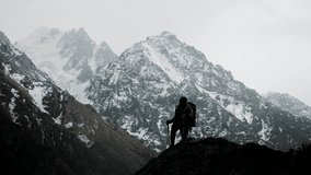 Silhouette of a hiker climbing a rocky mountain ridge with trekking poles against dramatic snowy peaks in outdoor alpine nature. - Powered by Shutterstock - Get 15% off with code: PIKWIZARD15
