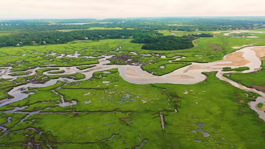 Expansive marsh system captured in aerial view shows tidal waterways winding through lush grasses, reflective pools dotting the surface, and natural shapes spreading across the horizon.