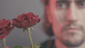 Close-Up of a Vibrant Red Rose with Water Droplets and Blurred Background of Serious Man in Warm Lighting - Powered by Shutterstock - Get 15% off with code: PIKWIZARD15