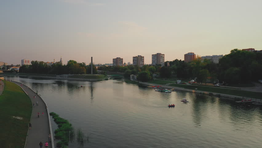 Aerial evening view of Orel city in Russia with river, Strelka, main buildings, churches and roads. Beautiful cityscape with lights reflecting on water at sunset, showing urban architecture, skyline.