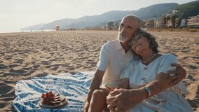 Affectionate elderly couple enjoying a romantic moment together during a picnic on a sandy beach at sunset, showing love, tenderness, and a happy retirement lifestyle by the sea - Powered by Shutterstock - Get 15% off with code: PIKWIZARD15