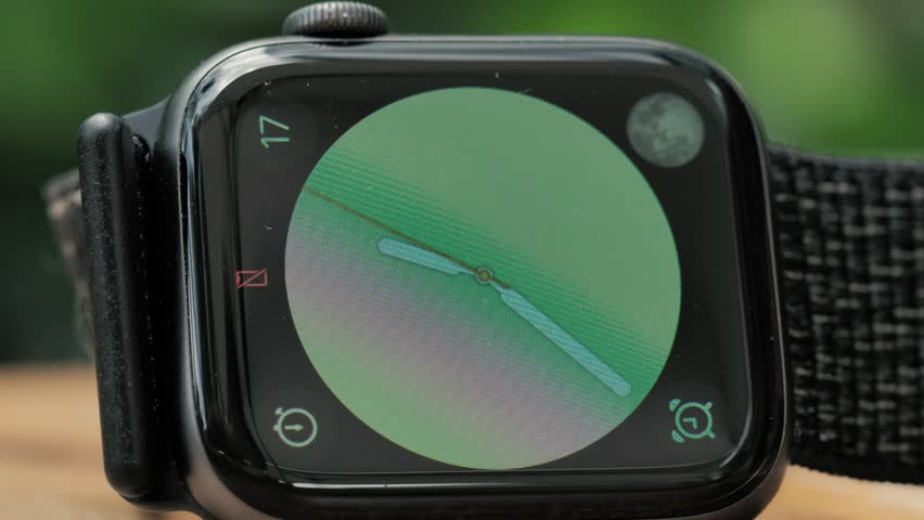 Black smartwatch on a table is showing a green clock.