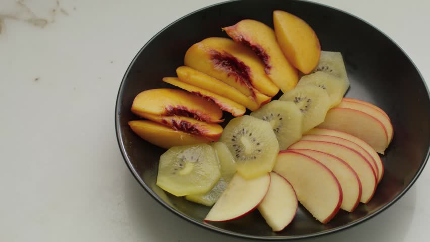 Very close view of a black bowl served with yogurt with slices of assorted fruit such as peach, kiwi and apple.