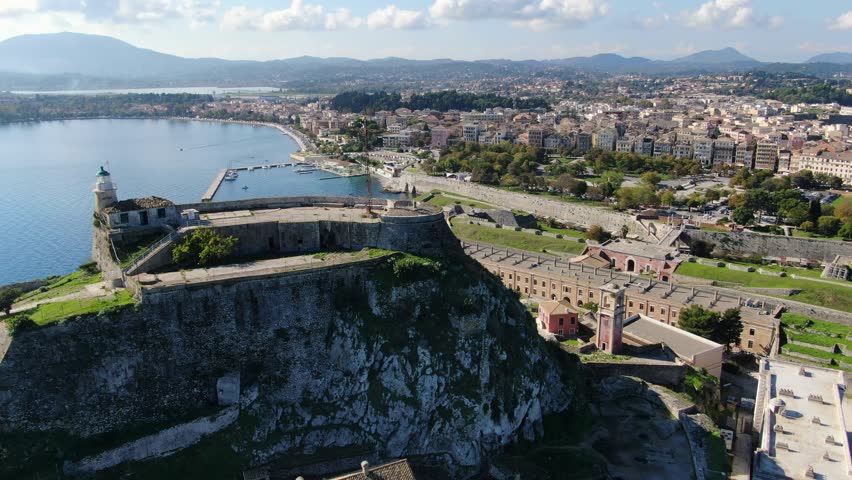 Aerial drone shot orbiting the lighthouse on the peak of the Old Venetian Fortress in Corfu, Greece, overlooking the Ionian Sea and city