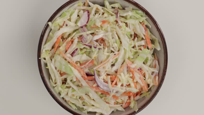 Coleslaw salad in a white bowl with cabbage, carrots on light surface zoom top
