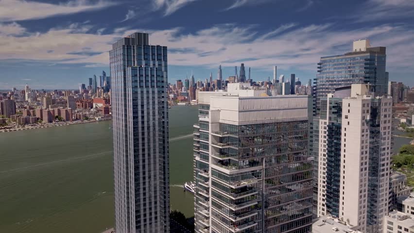 A cinematic drone shot rotating and rising above modern Brooklyn high-rise apartment buildings, revealing the Manhattan skyline and the iconic Empire State Building in the distance, of New York City.