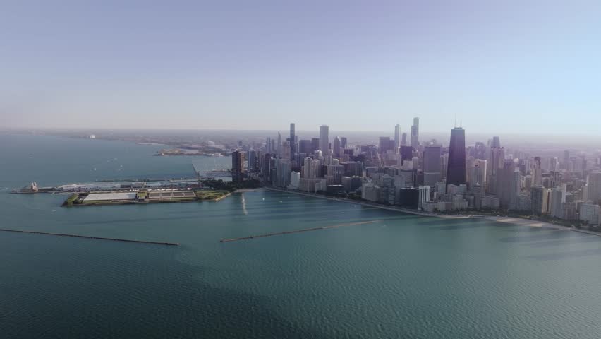 A high and wide, cinematic drone shot, flying far over Lake Michigan, slowly descending and moving forward toward Navy Pier, and the sprawling metropolis and unique urban landscape of Chicago, IL.