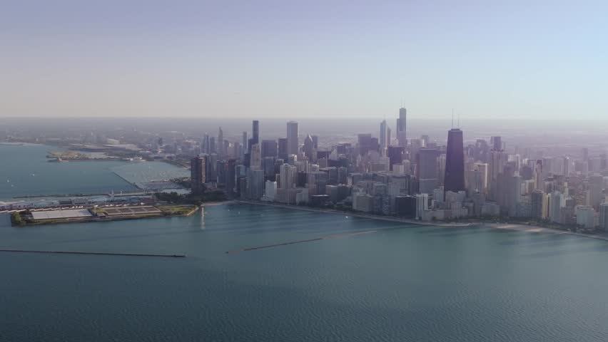 A high and wide, cinematic drone shot, captured far over Lake Michigan, slowly ascending and reversing, revealing Navy pier and the sprawling metropolis and unique urban landscape of Chicago, IL.