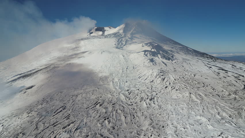 High angle aerial view of smoke billowing from Mount Etna, the most active volcano in Europe (with slopes covered in snow, Winter season)