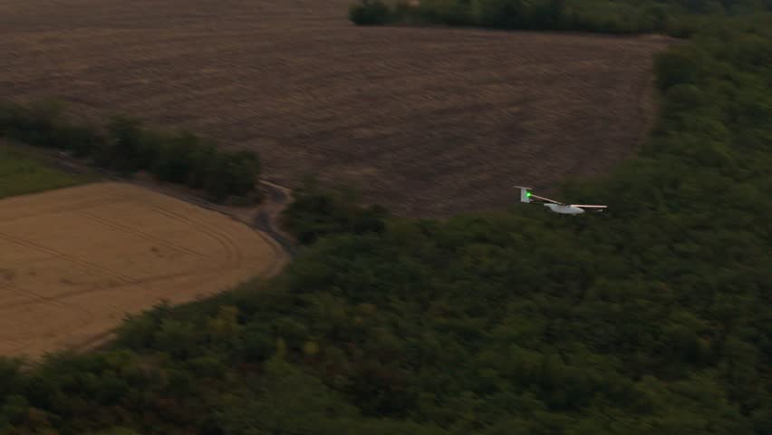 Aerial tracking shot of fixed wing drone flying above green forest with motion blur background
