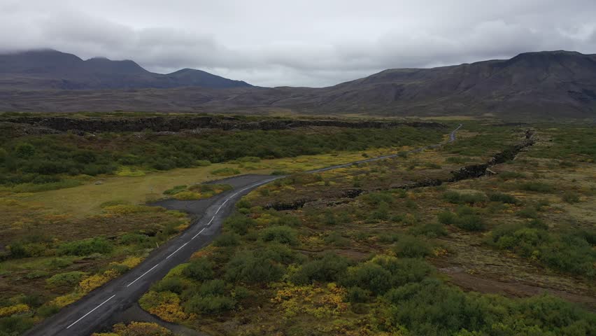 Aerial view of road cutting through a landscape with fissures, a scene of geological drama under a cloudy sky, Grindavik, Grindavíkurbær, Iceland.