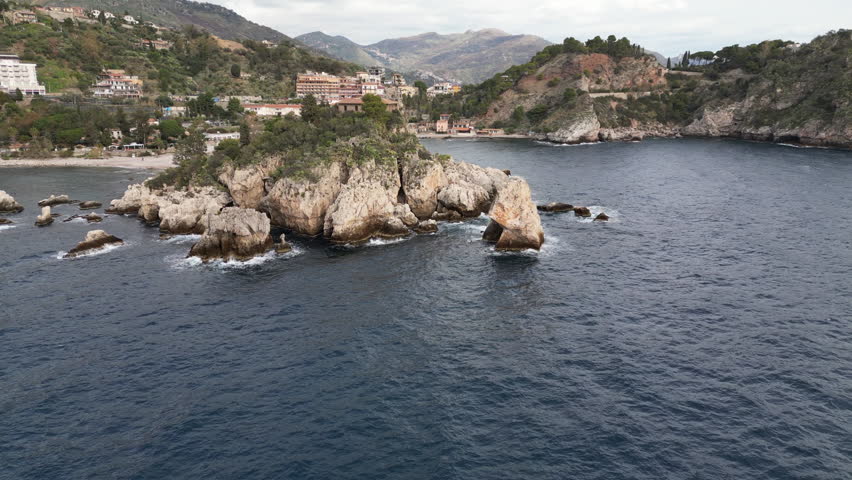 Drone flight towards Isola Bella, a small peninsula with rocky cliffs and beautiful beaches near Taormina, natural landscapes and holiday destination Sicily Italy
