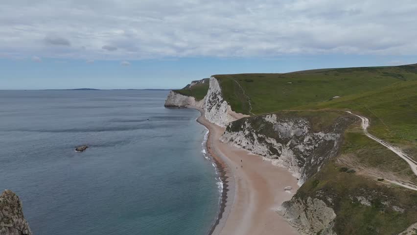 Aerial view of the rugged Durdle Door coast, showcasing dramatic white cliffs meeting the tranquil blue sea with a sandy beach, Lulworth, United Kingdom.