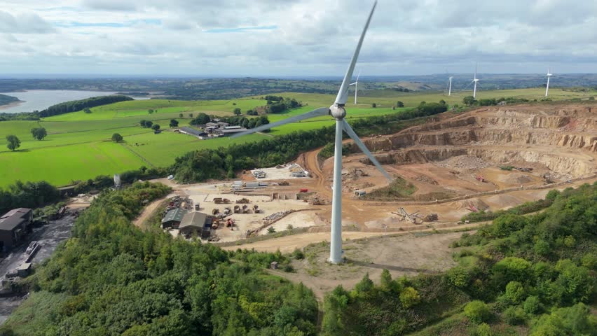 Aerial drone shot showing renewable energy turbines, quarry site, and Carsington countryside with blue lake and farmland in England