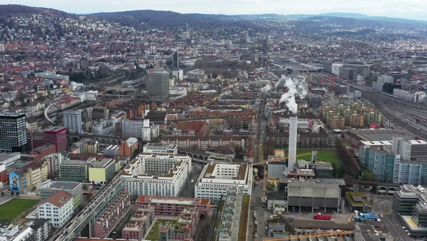 Aerial view of the city with a tall smokestack and railway tracks winding through the urban landscape, Zurich, Zurich, Switzerland.