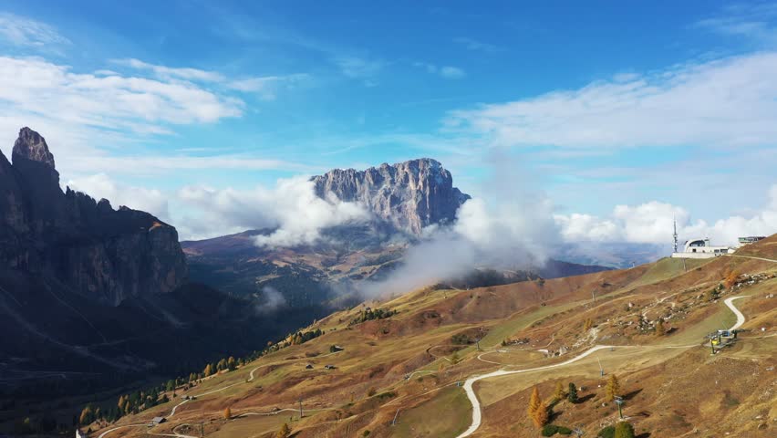 Aerial view of majestic rocky mountains partially covered with clouds creating a stunning contrast against the sky, Trentino-South Tyrol, Italy.