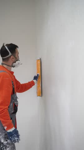Construction Worker Smoothing Fresh Plaster on Wall Using Roller and Spatula in Renovation Process Vertical
