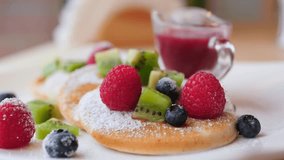 Close up of sweet honey or maple syrup pouring over a stack of freshly made pancakes, garnished with raspberries, blueberries, kiwi slices, and powdered sugar for a delicious breakfast - Powered by Shutterstock - Get 15% off with code: PIKWIZARD15