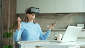 Senior gray haired female plays a game using VR glasses in virtual reality simulator while sitting at the table in kitchen at home. Elderly retired woman uses gestures to control computer programs - Powered by Shutterstock - Get 15% off with code: PIKWIZARD15