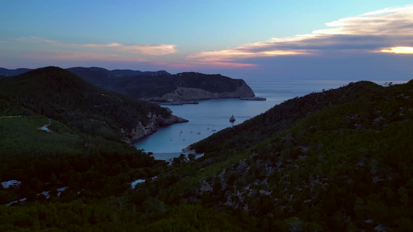 Ibiza Cala Benirras bay coastline at sunset. Smooth aerial view flight drone