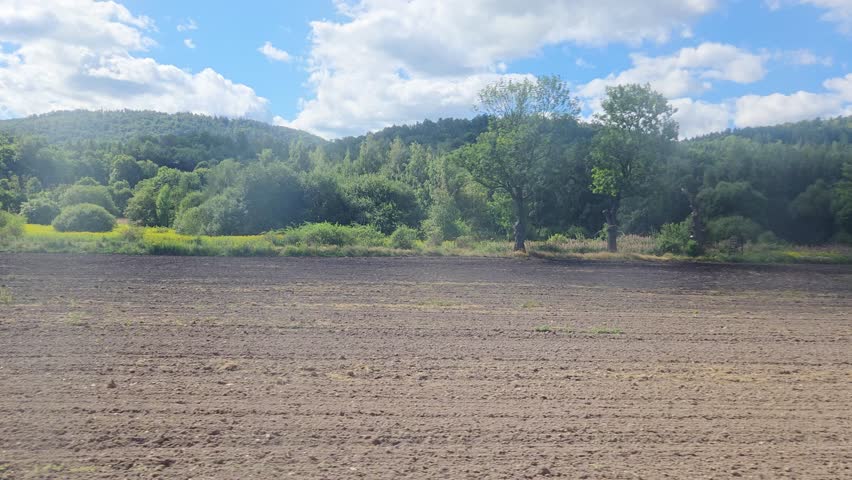 Tranquil Countryside Landscape with Plowed Field and Lush Green Hills