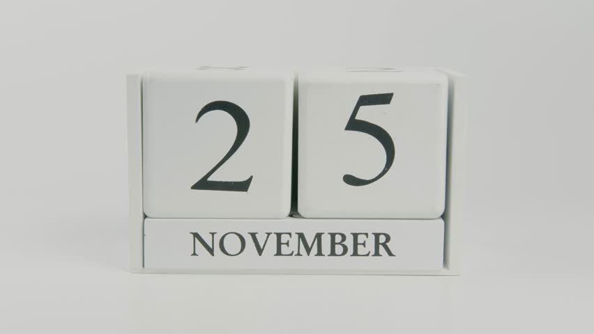 Hand flips a wooden white calendar, changing the date from November 25 to 26, on a clean white background. Perfect for time, schedule, and holiday concepts