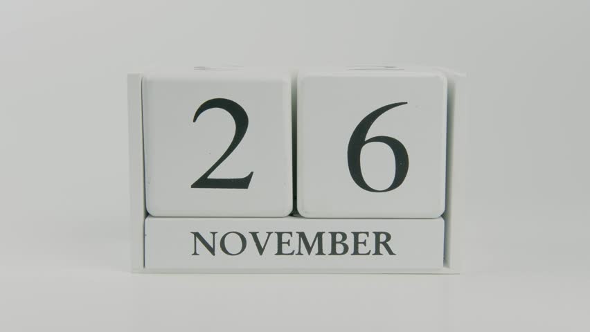 Hand flips a wooden white calendar, changing the date from November 26 to 27, on a clean white background. Perfect for time, schedule, and holiday concepts