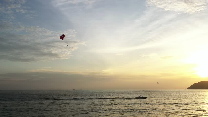 An exciting parasailing trip over the sea during a beautiful sunset at the coastal location of Langkawi Island at sunset. Malaysia