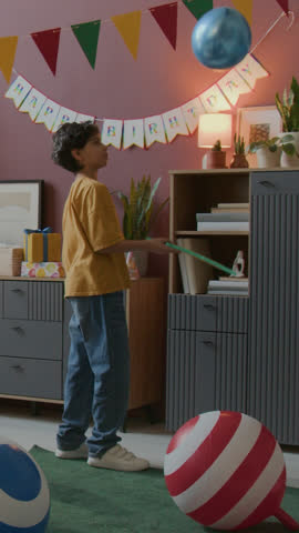 Vertical shot of little boys playing with colorful balloons in decorated for birthday party, children room