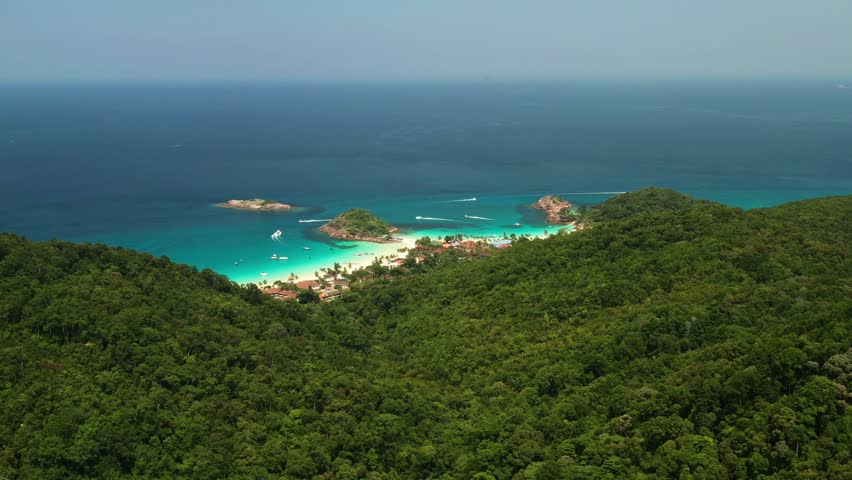 A tropical beach behind a hill in the popular resort of Redang Island with clear turquoise waters and lush greenery. Malaysia