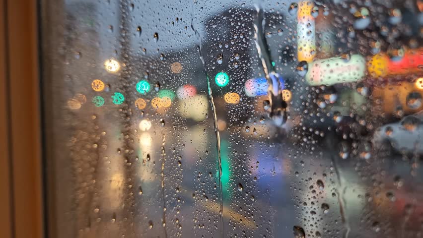 Macro shot of rain droplets running down glass with warm light reflections. Perfect for intro scenes, aesthetic background, or romantic visuals.