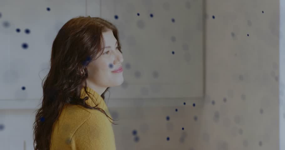 Woman watching drifting blue dots forming spiral in studio, turning and smiling for technology demo. Abstract, futuristic, dynamic, innovation, artistry, digital, creativity