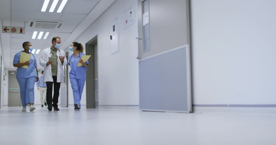 Doctor leading nurses hospital hall reviewing notes as animated charts appearing passing wheelchair. Medical, teamwork, futuristic, technology, healthcare, professionalism, collaboration