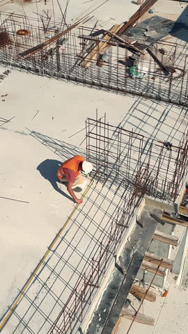 Construction worker measuring rebar framework on building structure. A construction worker in safety gear measures steel rebar , viewed from above.